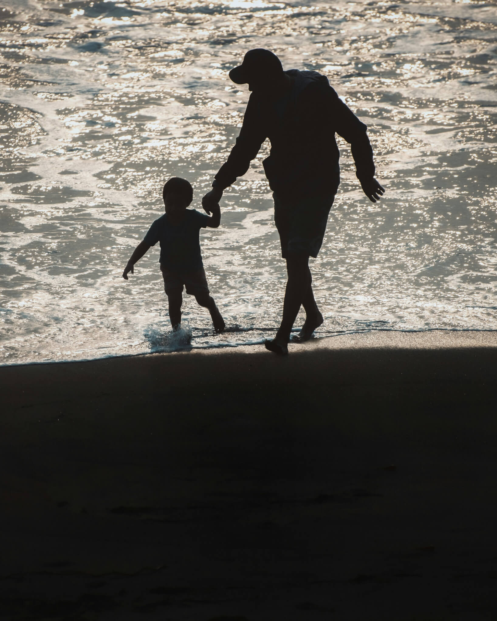 Adult and child walking hand in hand along the shoreline at golden hour