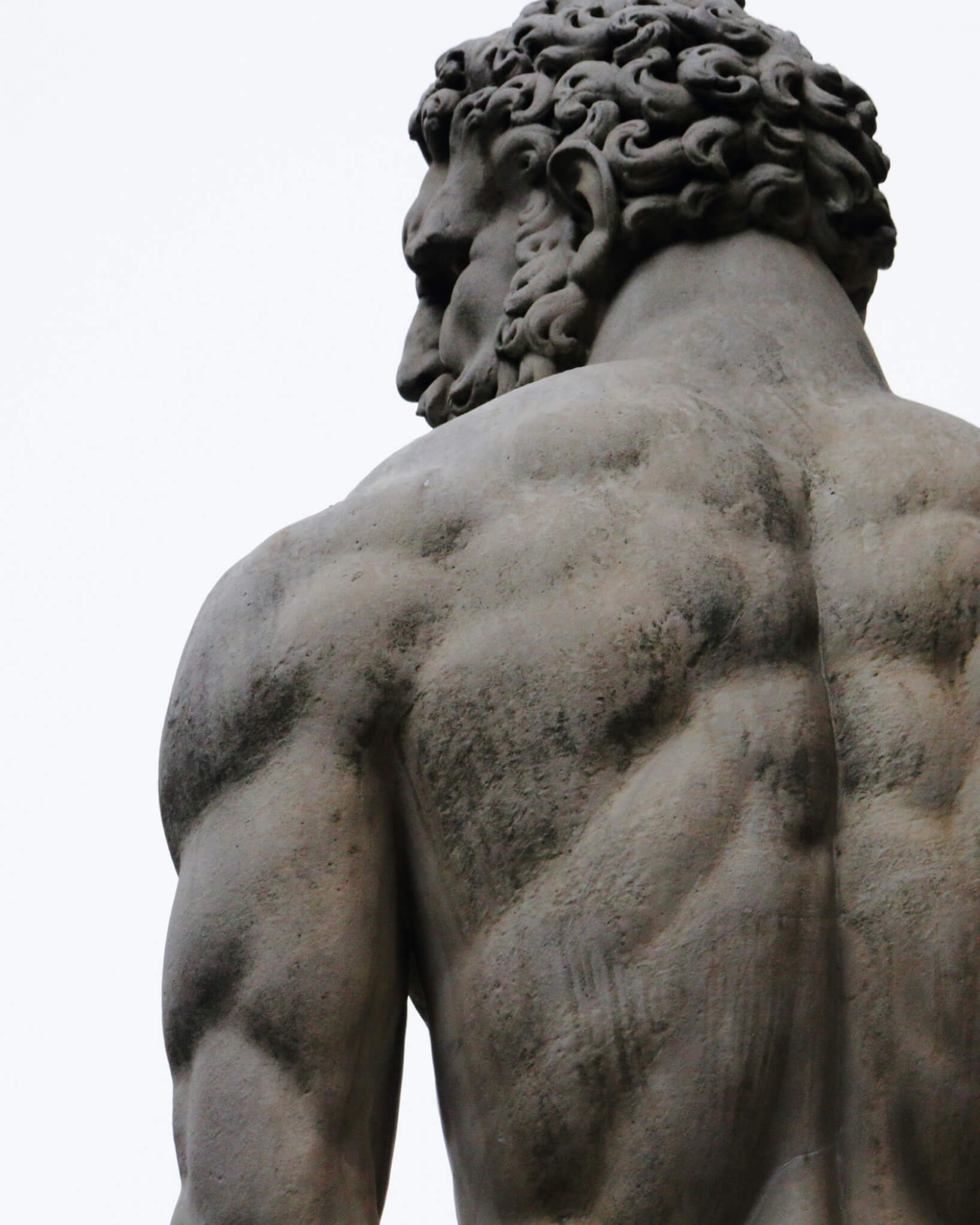 Stone statue of a powerful figure seen from behind, strength carved and enduring