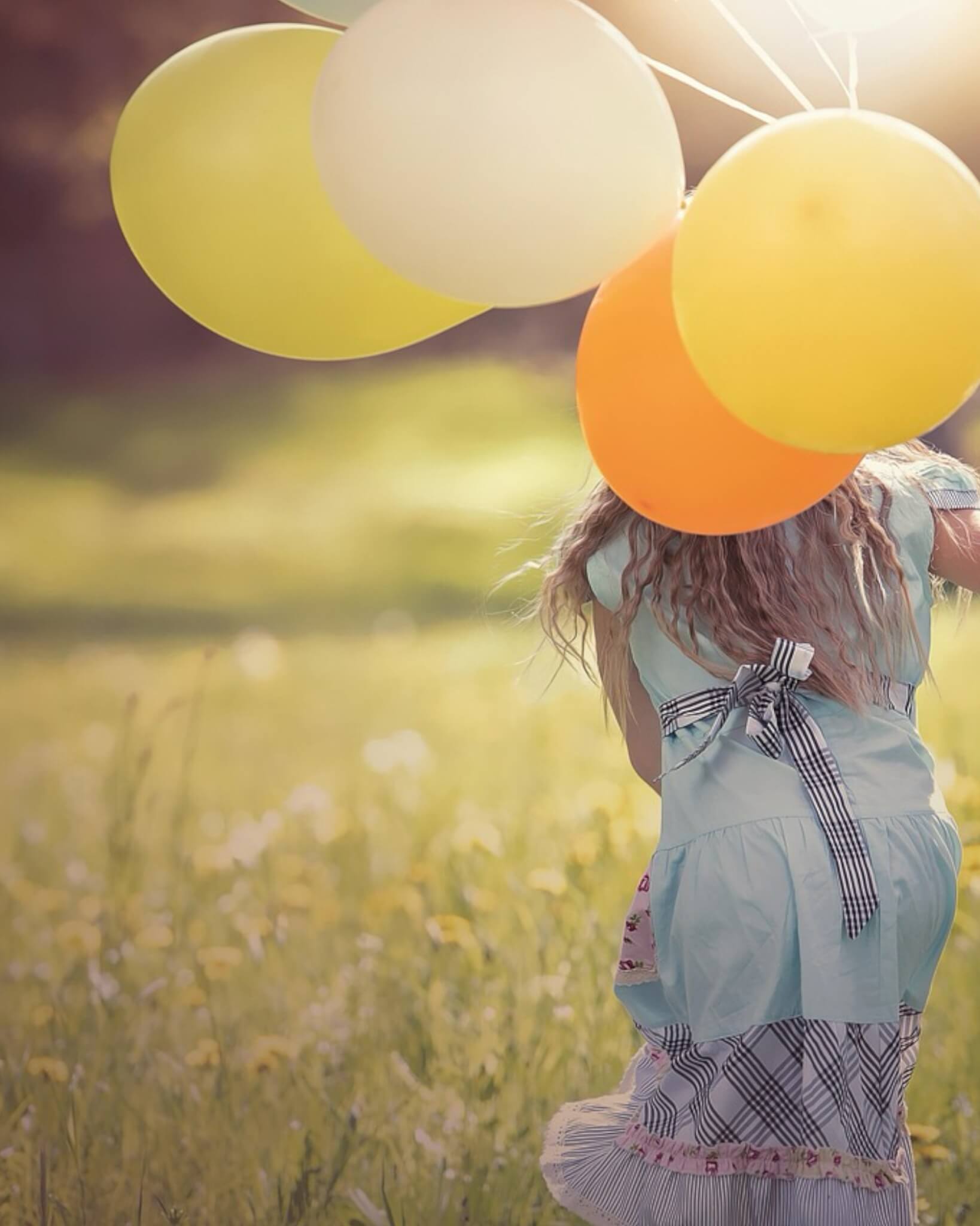 A child running through a sunlit meadow with colourful balloons
